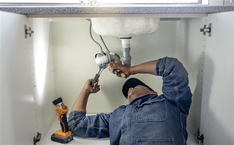 Plumber repairing pipes beneath a bathroom sink in Lake Worth Beach