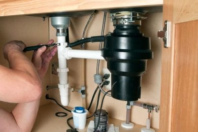 Plumber repairing a garbage disposal beneath a kitchen sink in Lake Worth Beach