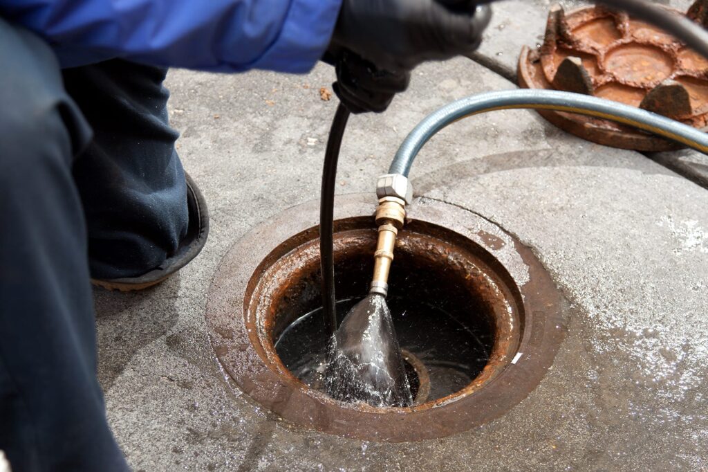 Plumber hydro jetting a sewer line through a manhole in Lake Worth Beach