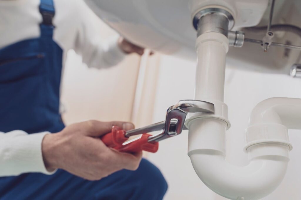 Plumber repairing a white drain pipe beneath a sink in Lake Worth Beach