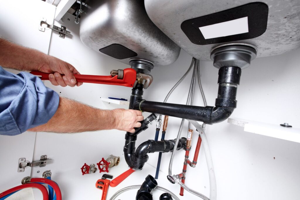 Plumber repairing drain pipes beneath a kitchen sink in Lake Worth Beach