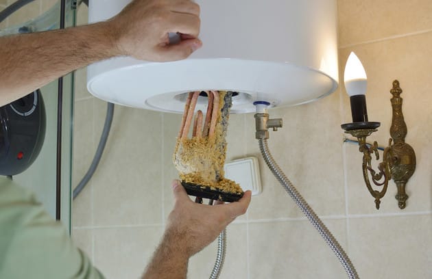 Technician removing mineral buildup from a water heater in Lake Worth Beach